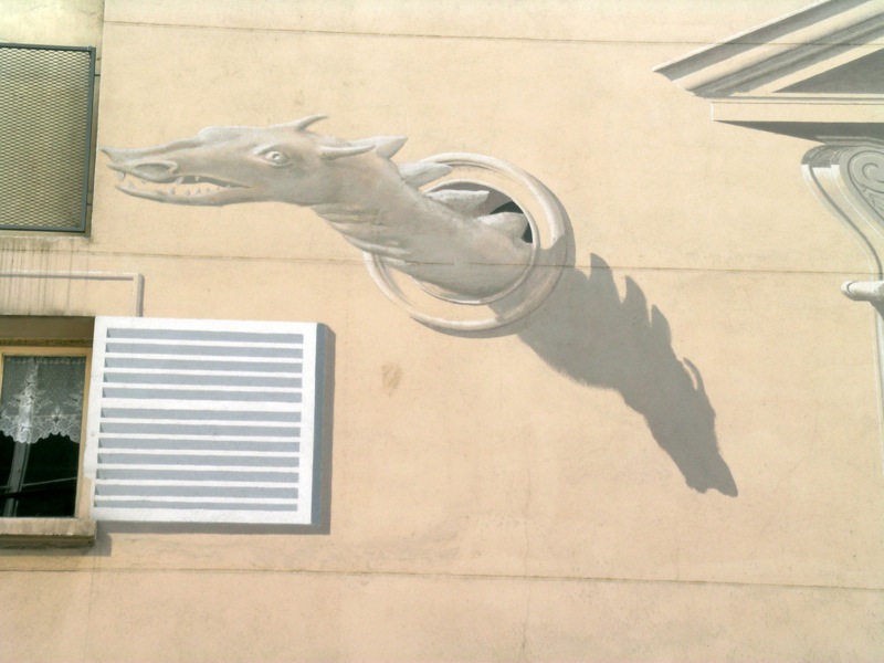 Détail de l’anamorphose du Théâtre Saint Georges. Vu de face, tel qu’il est peint, le dragon est déformé de façon calculée comme tout le relief de la façade »