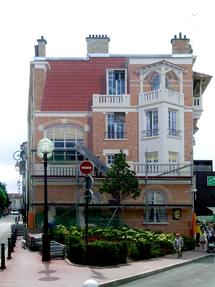 Façade d'immeuble entièrement peinte en trompe-l'œil, échafaudage encore en place au rez-de-chaussée.
